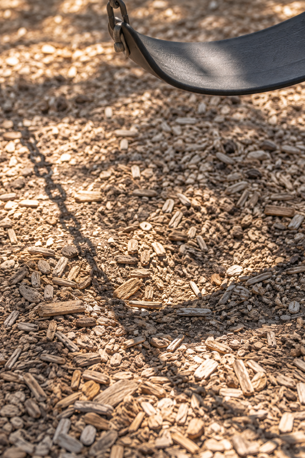 Textured wood-chip ground and swing seat in warm sunlight, portrait photo